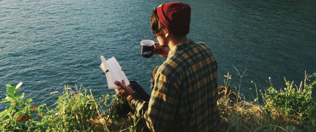 Man reading at the edge a lake with a cup of coffee